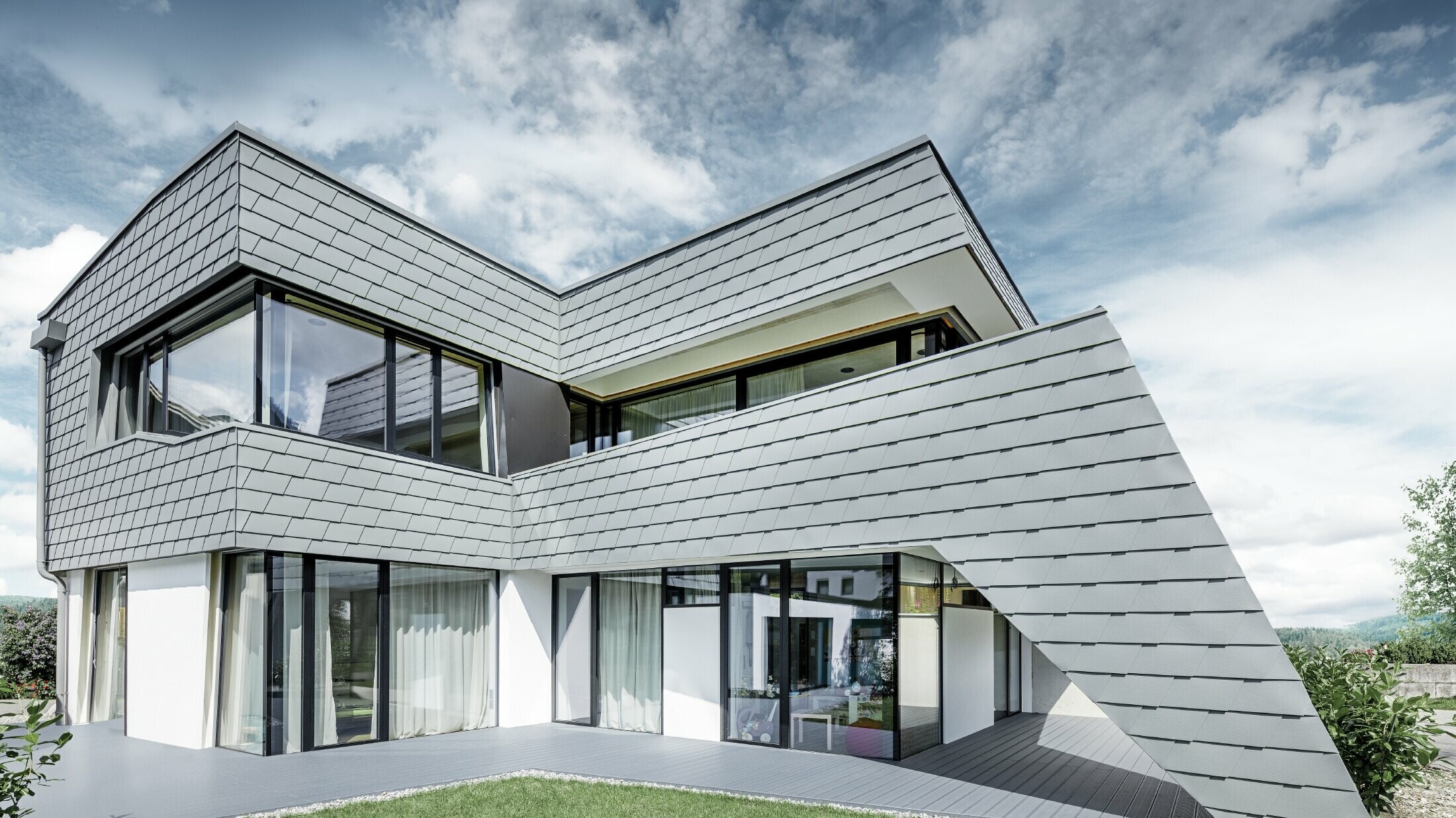 Sodobna enodružinska hiša z ravno streho, velikimi okni in fasado iz aluminijastih skodel PREFA v svetlo sivi barvi