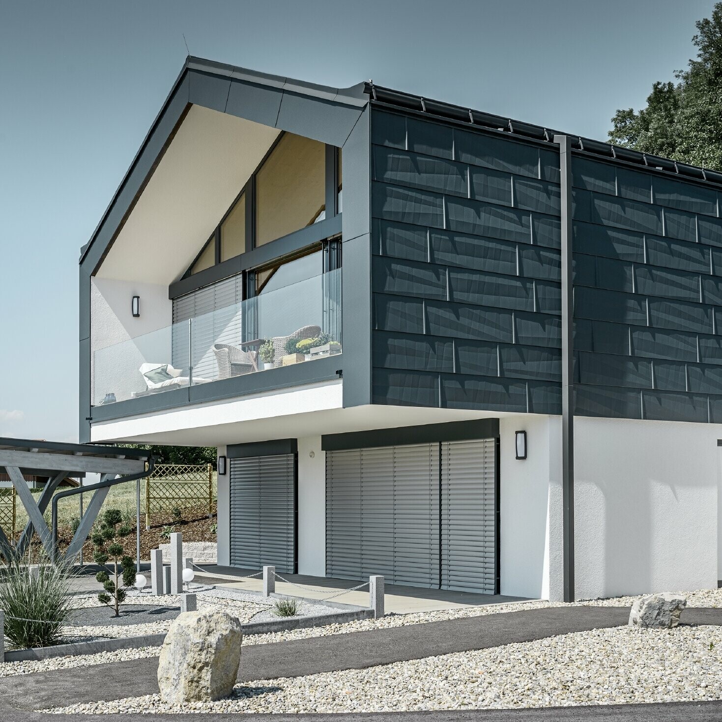 Sodobna večdružinska hiša z velikimi steklenimi površinami, streha in fasada sta bili obloženi s strešnimi in fasadnimi paneli FX.12 PREFA v antracitni barvi.