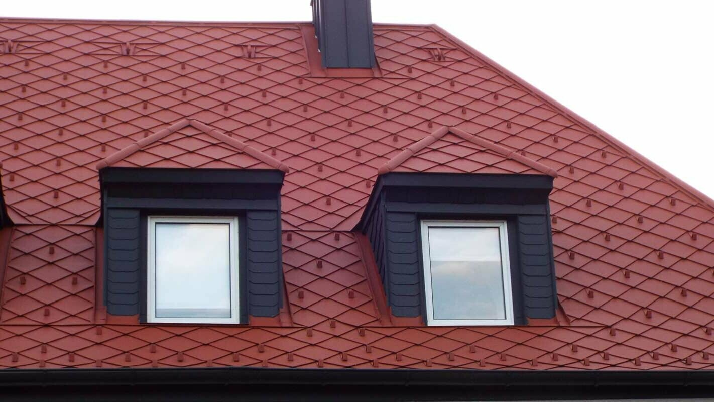Obnova strehe s čopastimi dvokapnimi površinami nad mansardnimi okni s strešnimi rombi PREFA v videzu opečnate kritine