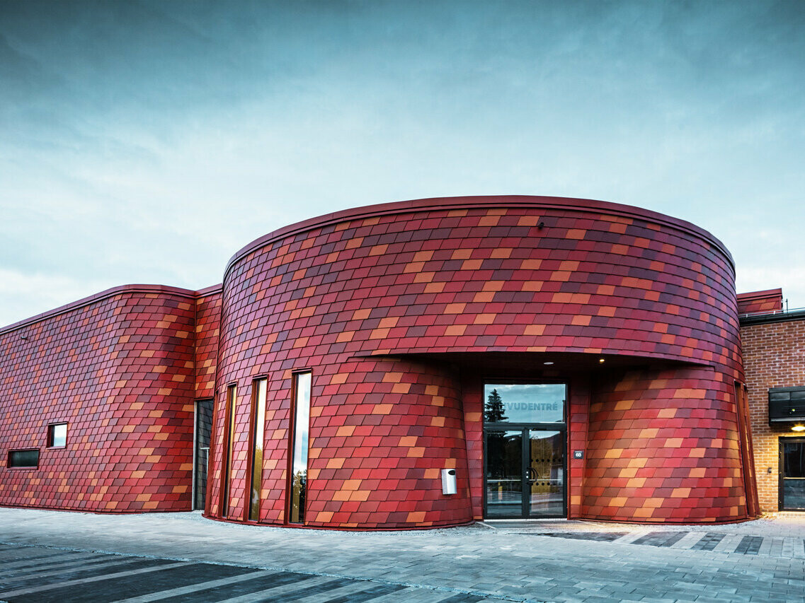 Pogled spredaj na dvorano za led in dogodke na Švedskem. Oksidirajoče rdeče strešnike se popolnoma prilegajo zaobljenosti zgradbe.