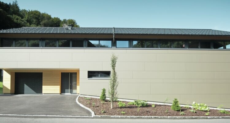 Dolga hiša s strešno ploščo PREFA v antracitni kritini P.10 v kombinaciji s kompozitno ploščo PREFA v bronasti barvi na fasadi; sodoben slog gradnje v kombinaciji z ozkimi okni in leseno fasado.