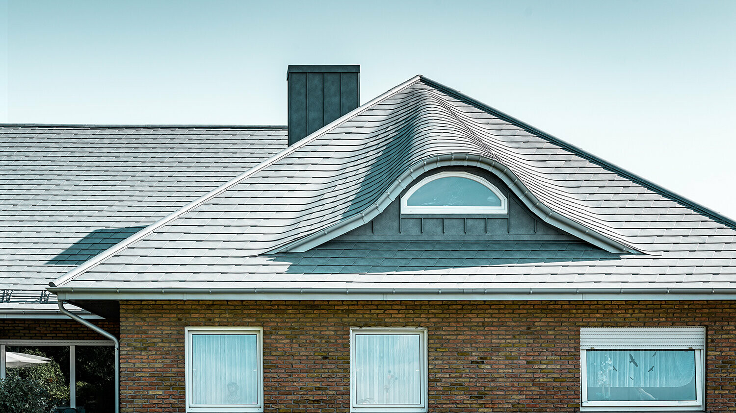 Enodružinska hiša iz 70-ih let prejšnjega stoletja s streho iz aluminijastih strešnih skodl v barvi P.10 kamnito siva z vijugasto zaobljeno frčado z okroglim oknom