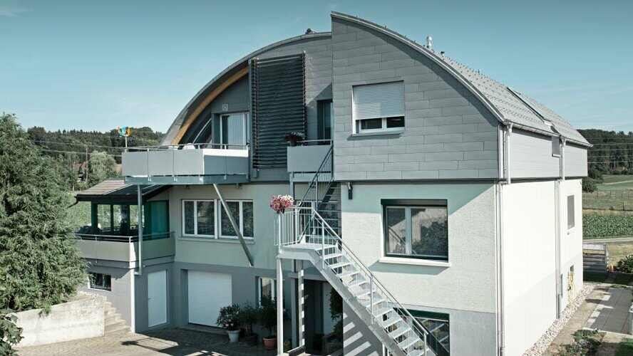 Stanovanjska hiša z valjasto streho prekrito s strešnimi ploščami PREFA in Prefalz v barvi P.10 svetlo siva