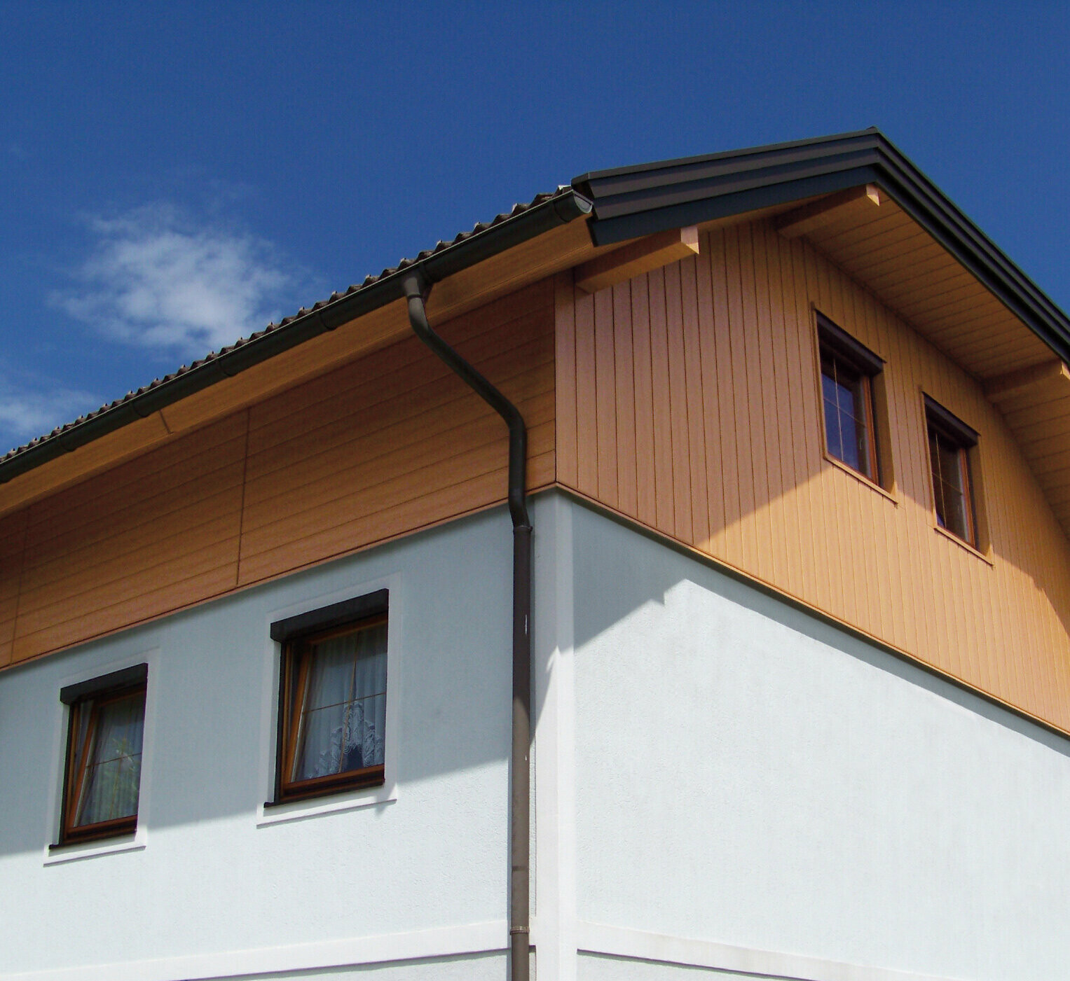 Velika družinska hiša s streho z delnimi čopi in oblogo zatrepa s PREFA Sidings v videzu lesa (barva naravni hrast)