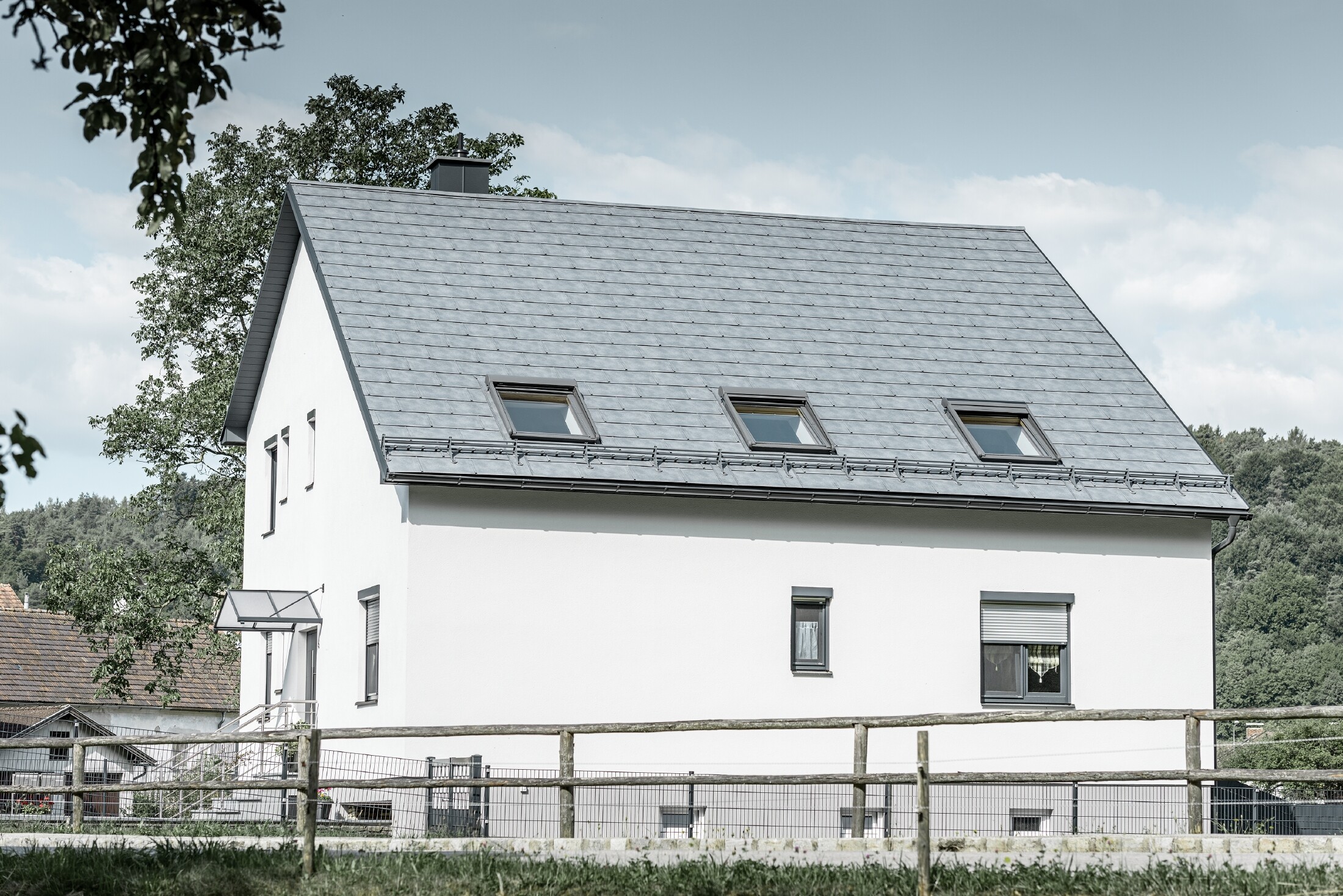 Das Satteldach des klassischen Einfamilienhauses wurde mit der neuen PREFA Dachplatte R.16 in Steingrau eingedeckt. In der Dachfläche wurden drei Dachfenster eingefügt und Schneerechen montiert. Die Fassade ist einfach in Weiß gehalten.