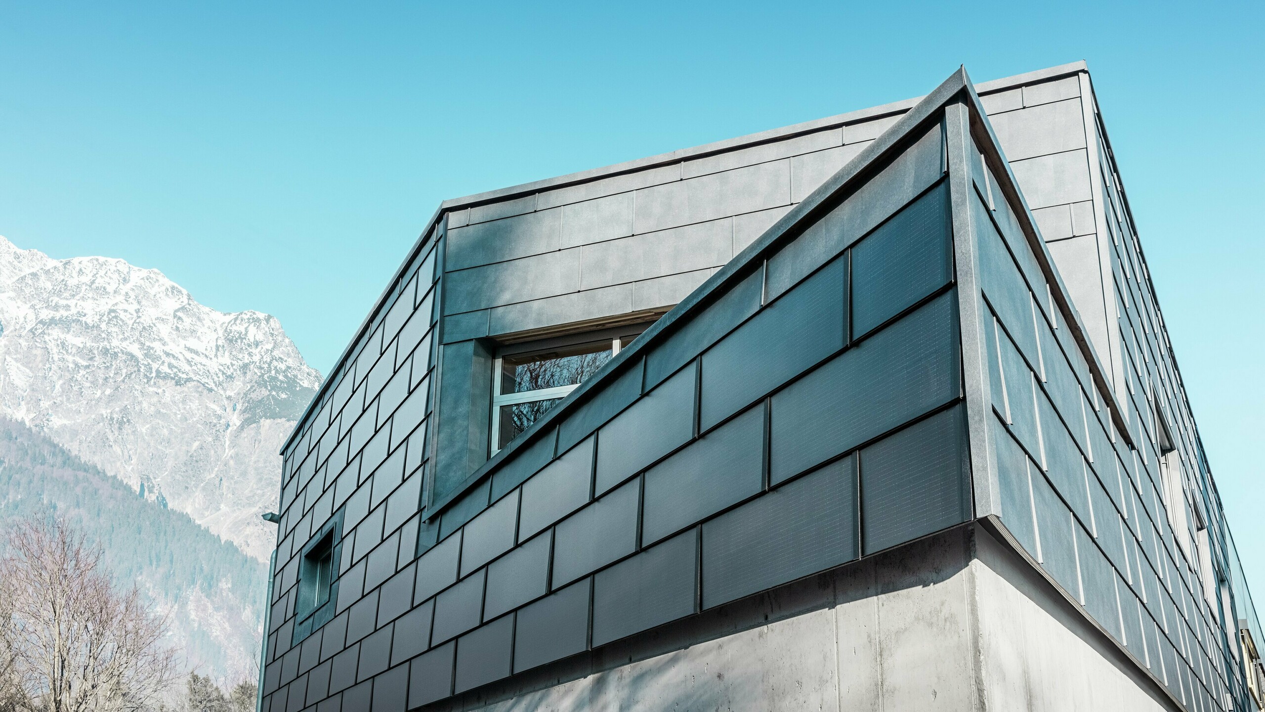 Moderna fasada stavbe s solarnimi strešnimi ploščami PREFA: trajnostne aluminijaste plošče z vgrajeno fotovoltaiko proizvajajo električno energijo in se harmonično vklapljajo v arhitekturno zasnovo.
