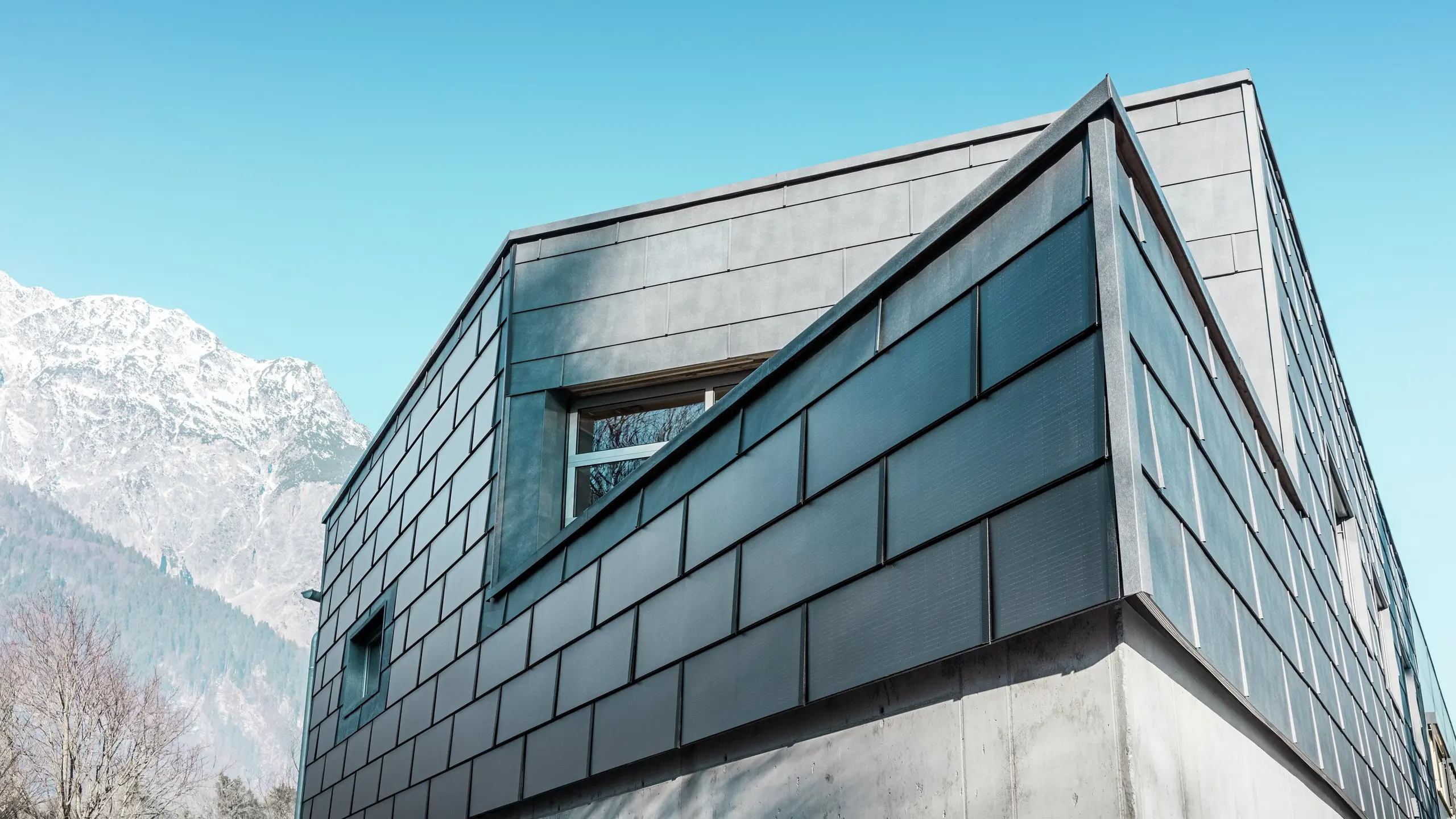 Moderna fasada stavbe s solarnimi strešnimi ploščami PREFA: trajnostne aluminijaste plošče z vgrajeno fotovoltaiko proizvajajo električno energijo in se harmonično vklapljajo v arhitekturno zasnovo.
