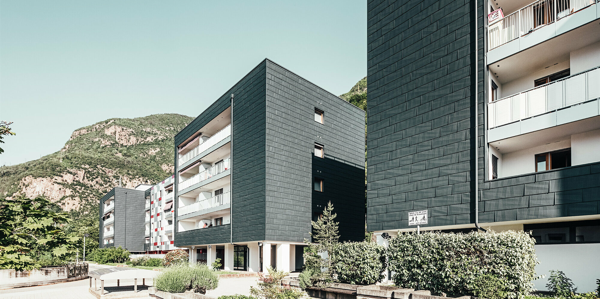 Ansicht von schräg vorne auf den sanierten Wohnbau in Bozen. Balkone mit weißem Geländer und Hausfassade realisiert mit dem Produkt Fassadenpaneel FX.12.