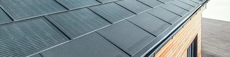 Solarna strešna plošča PREFA v veliki izvedbi v kombinaciji s strešno ploščo R.16 v črni barvi, pravokotnim žlebom in fasado iz macesnovega lesa