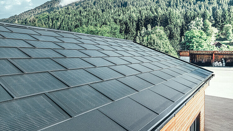 Solarna strešna plošča PREFA v veliki izvedbi v kombinaciji s strešno ploščo R.16 v črni barvi, pravokotnim žlebom in fasado iz macesnovega lesa