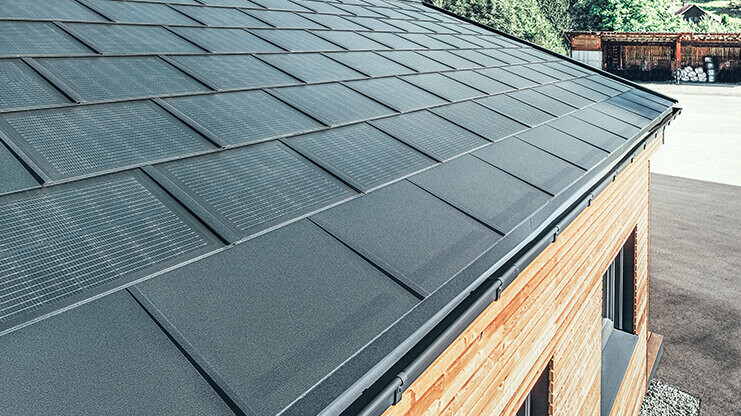 Solarna strešna plošča PREFA v veliki izvedbi v kombinaciji s strešno ploščo R.16 v črni barvi, pravokotnim žlebom in fasado iz macesnovega lesa
