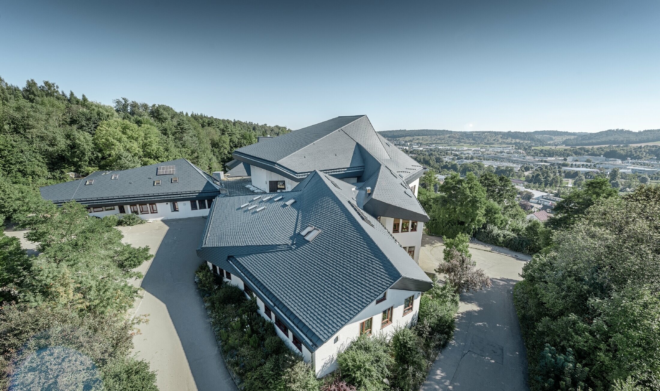 Valdorfska šola v Heidenheimu z novo sanirano streho; velika strešna površina z veliko koti in nakloni je pokrita s strešnimi skodlami PREFA v antracitni barvi