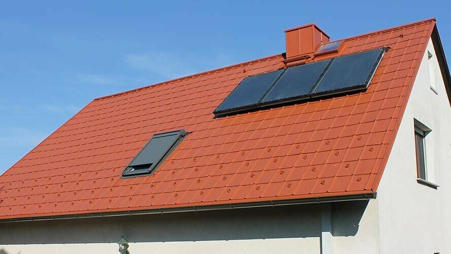 Samostojna hiša s dvokapno streho, prekrito s strešnimi ploščami PREFA v opečno rdeči barvi. Strešna površina s solarnim sistemom in strešnim oknom