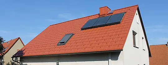 Samostojna hiša s dvokapno streho, prekrito s strešnimi ploščami PREFA v opečno rdeči barvi. Strešna površina s solarnim sistemom in strešnim oknom
