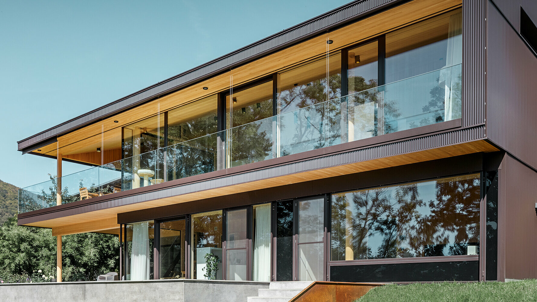 Nova enodružinska hiša z velikimi steklenimi površinami in rjavo aluminijasto fasado