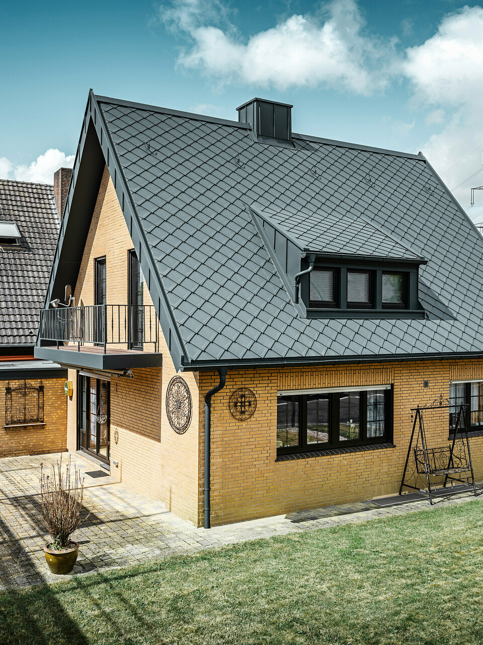 Enodružinska hiša v Tönisvorstu s PREFA streho s strešnimi rombi 29×29 v P.10 antracitni barvi, ki imajo izrazit karo vzorec. Mansarde, dimnik in vhodni prostor so obloženi s sistemom PREFALZ, ki skupaj z odtočno cevjo in visečim žlebom v P.10 antracitni barvi daje hiši brezčasen in eleganten videz. Opečna stavba z aluminijasto streho se sklada z mirno, zeleno okolico naselja.
