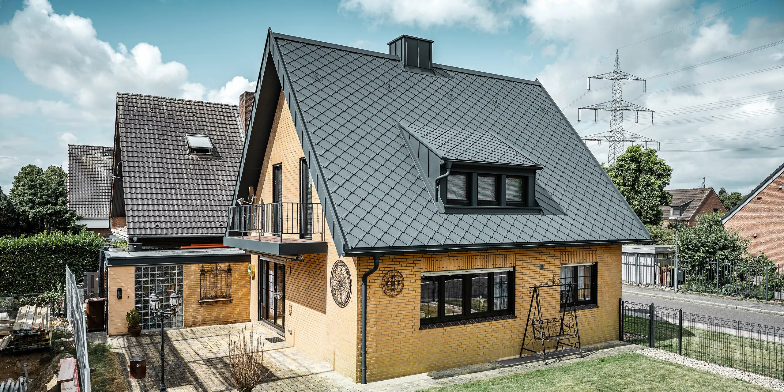 Enodružinska hiša v Tönisvorstu s PREFA streho s strešnimi rombi 29×29 v P.10 antracitni barvi, ki imajo izrazit karo vzorec. Mansarde, dimnik in vhodni prostor so obloženi s sistemom PREFALZ, ki skupaj z odtočno cevjo in visečim žlebom v P.10 antracitni barvi daje hiši brezčasen in eleganten videz. Opečna stavba z aluminijasto streho se sklada z mirno, zeleno okolico naselja.