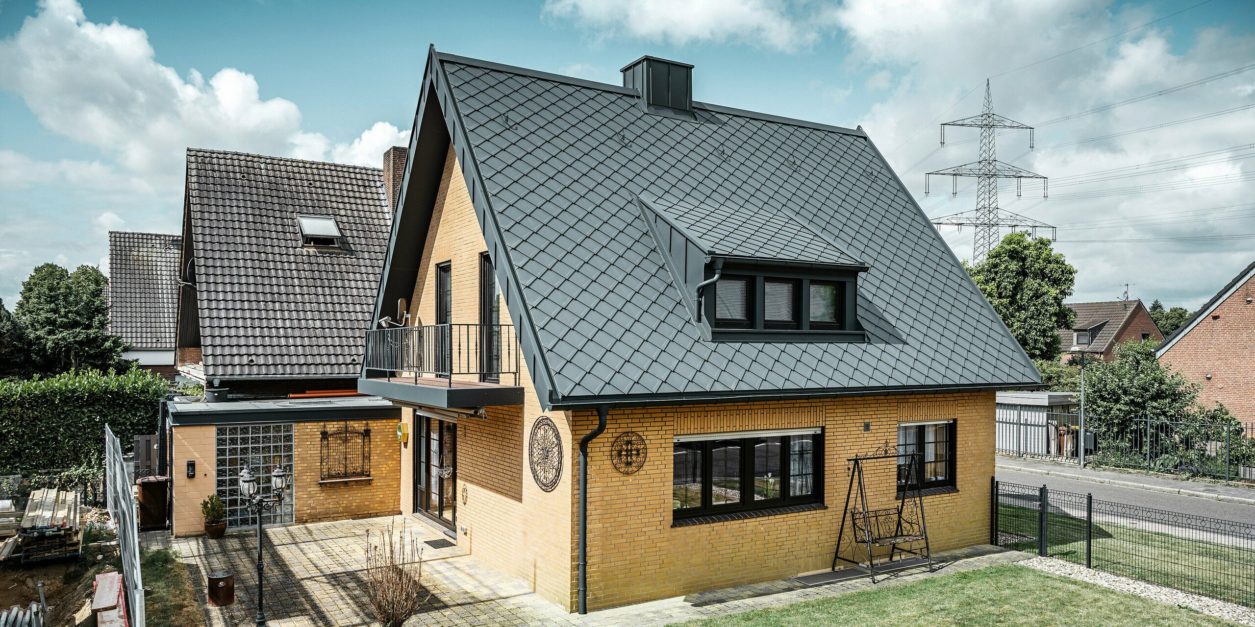 Enodružinska hiša v Tönisvorstu s PREFA streho s strešnimi rombi 29×29 v P.10 antracitni barvi, ki imajo izrazit karo vzorec. Mansarde, dimnik in vhodni prostor so obloženi s sistemom PREFALZ, ki skupaj z odtočno cevjo in visečim žlebom v P.10 antracitni barvi daje hiši brezčasen in eleganten videz. Opečna stavba z aluminijasto streho se sklada z mirno, zeleno okolico naselja.