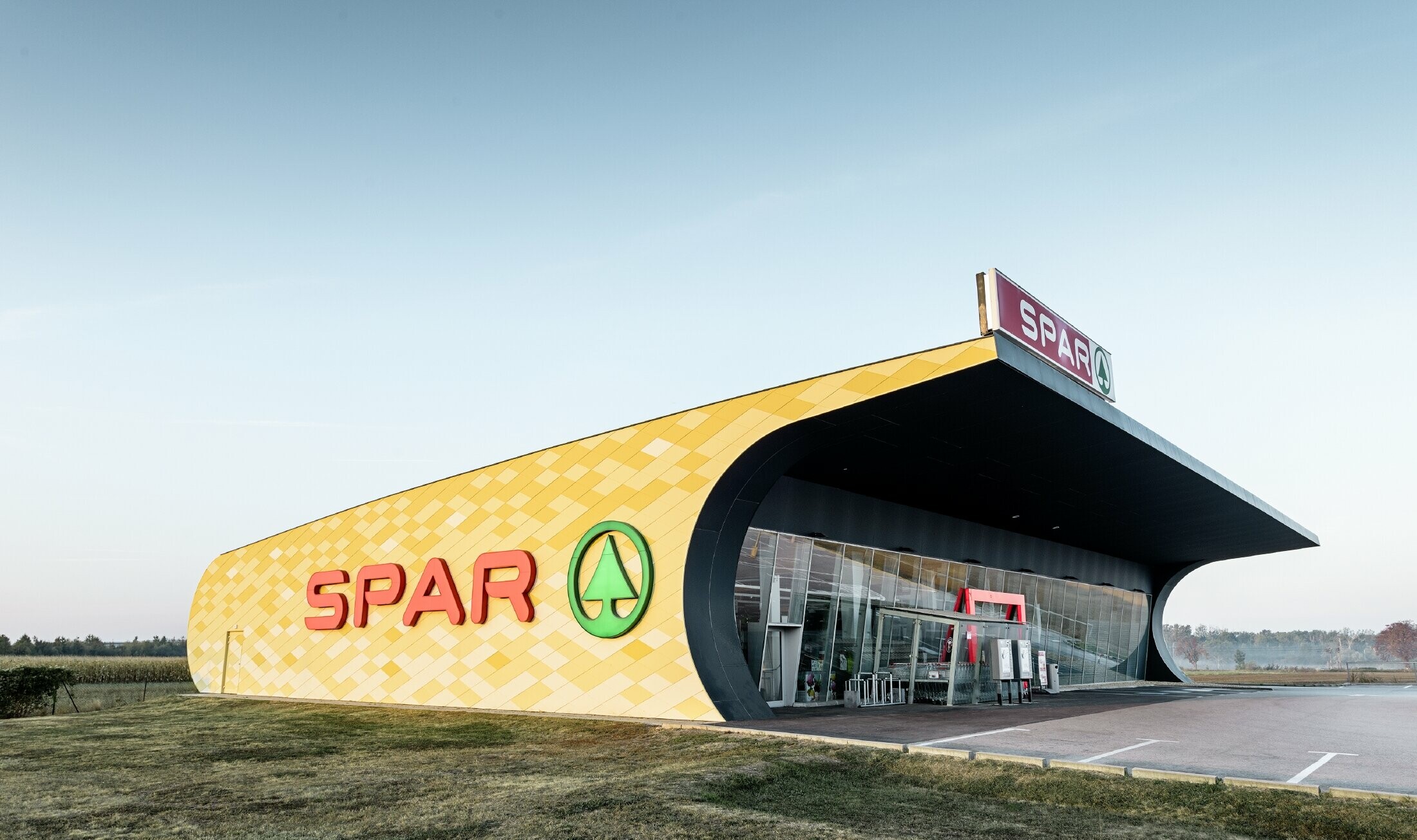 Podružnica Spar z aluminijasto fasado v rumeno-oranžnem karo vzorcu in logotipom Spar