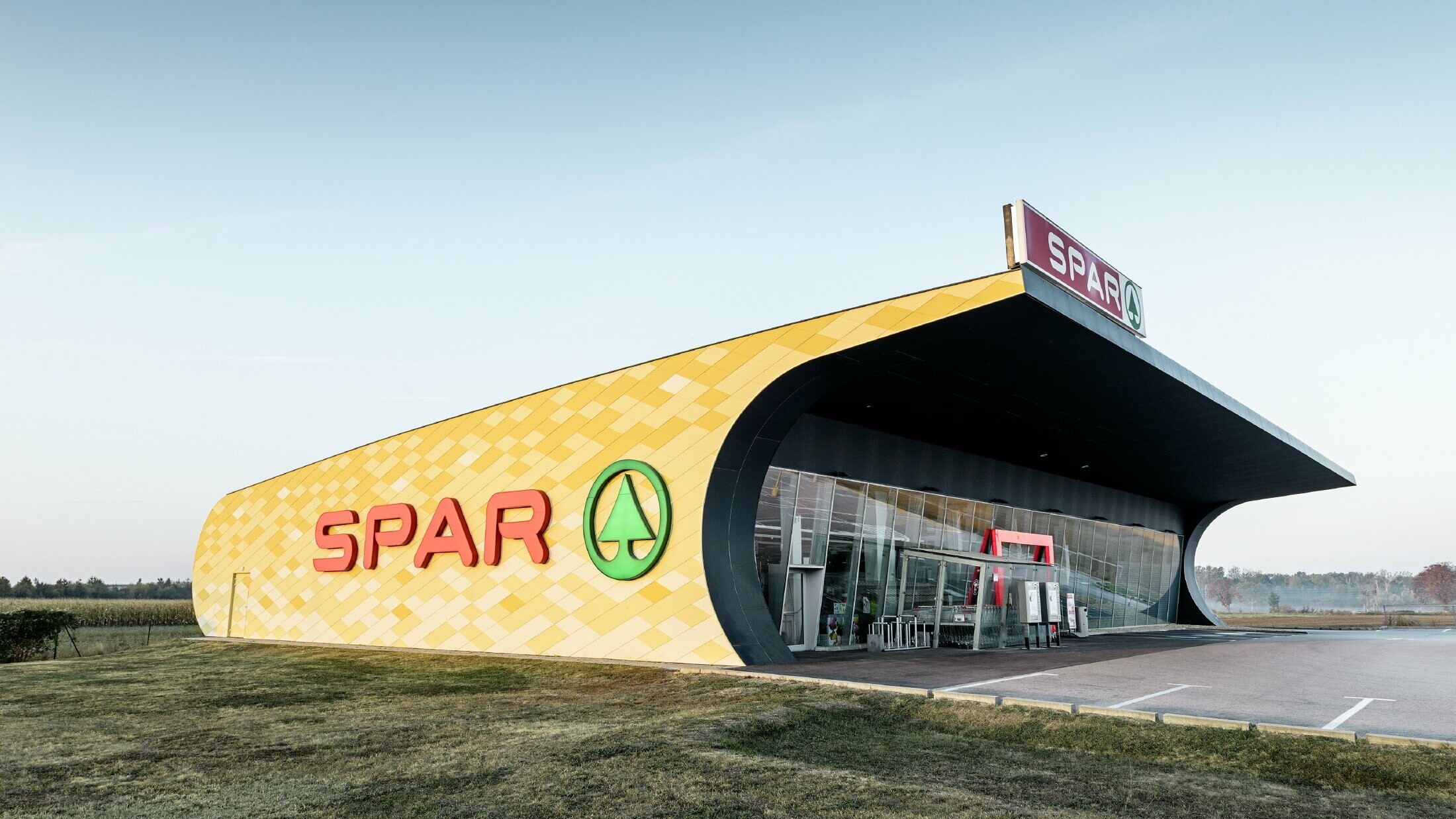 Podružnica Spar z aluminijasto fasado v rumeno-oranžnem karo vzorcu in logotipom Spar