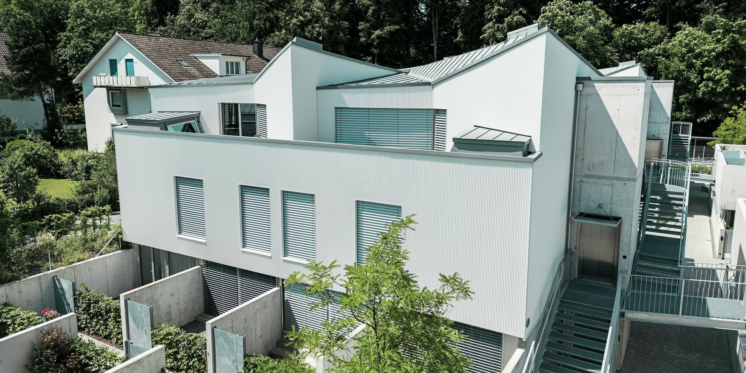 Vogelperspektive auf ein Ensemble moderner Tiny Homes in Zollikerberg mit PREFA Zackenprofil-Fassade in P.10 Reinweiß und PREFALZ Dächern in Patinagrau. Die klaren Linien und kontrastreichen Materialien verleihen dem Projekt eine markante Optik. Hochwertiges Aluminium sorgt für Langlebigkeit, Witterungsschutz und architektonische Präzision auf kleinstem Raum.