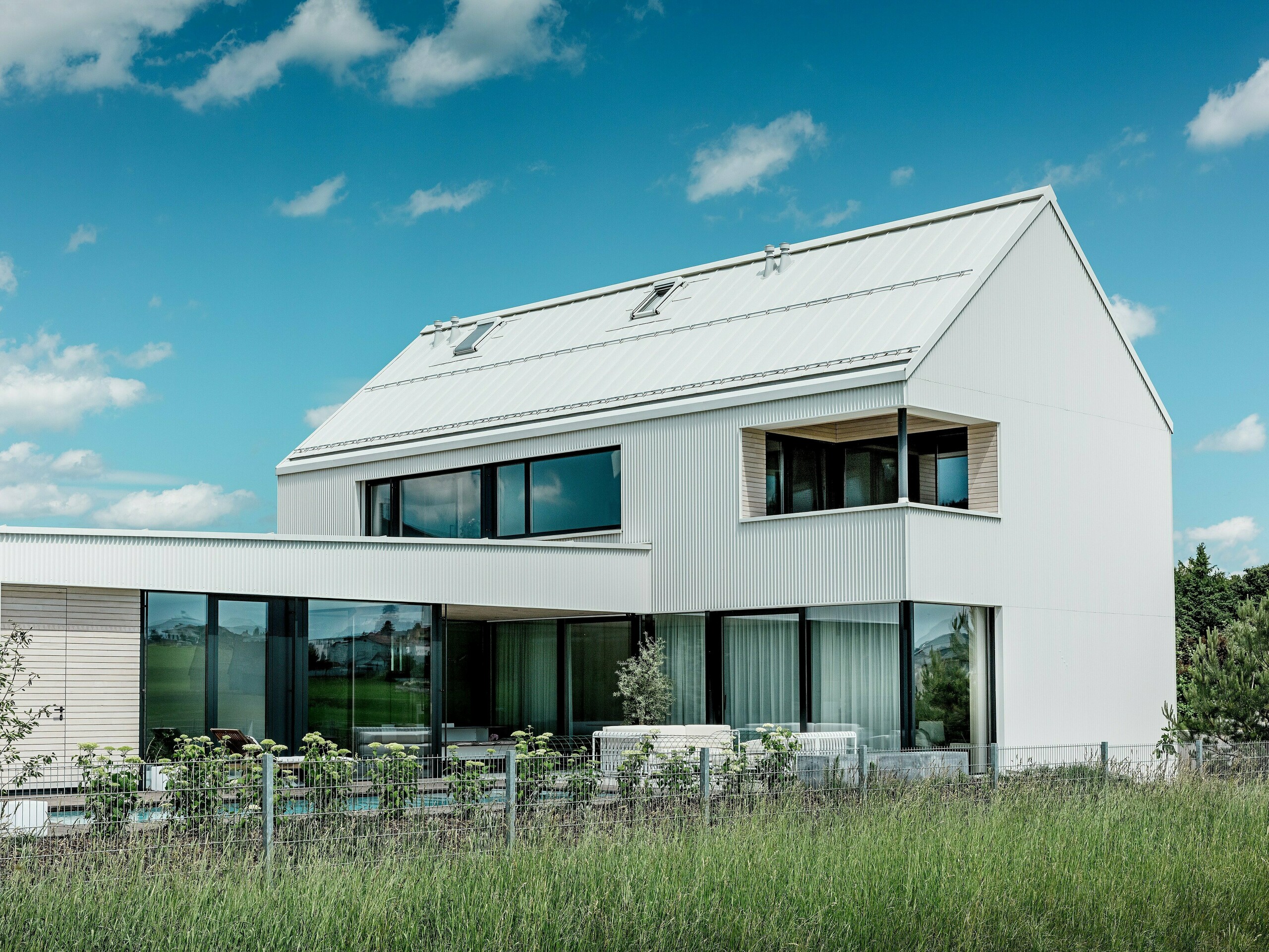 Ta impresivna enodružinska hiša v Freistadtu navdušuje s svojo elegantno arhitekturo, pri kateri je bil za fasado in streho uporabljen bel PREFALZ aluminij. Fasada s cik cak gubami ustvarja sodoben, geometričen videz, ki se harmonično vklaplja v naravno okolje. Velika okna ne prinašajo le veliko dnevne svetlobe v notranjost, ampak ponujajo tudi širok pogled na okoliško pokrajino. Strma dvokapna streha in moderni balkon z leseno oblogo poudarjata minimalističen dizajn in trajnostno gradnjo hiše. PREFALZ zagotavlja vizualno stabilnost in odpornost proti vremenskim vplivom ter zagotavlja dolgo življenjsko dobo z majhnimi stroški vzdrževanja.