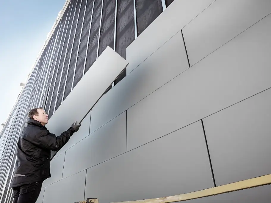 Fotografija delno dokončane fasade, obložene s sistemom PREFA Siding širine 500 mm. Klepar namešča naslednji fasadni panel. Posnetek je narejen od spodaj.