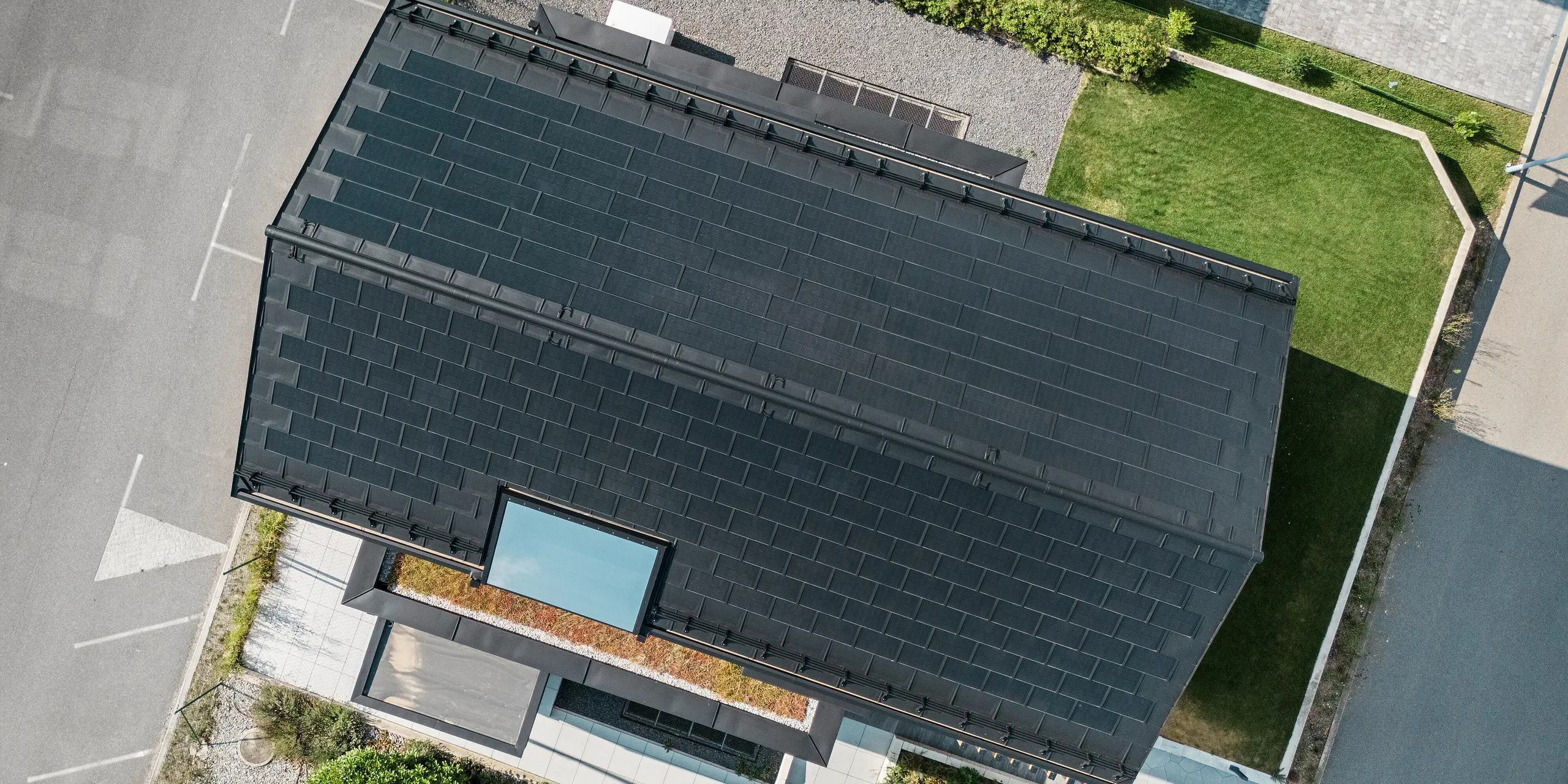 Pogled iz zraka na vzorčno hišo Autark v centru montažnih hiš Blaue Lagune v Vösendorfu (Avstrija). Streha je prekrita s črnimi solarnimi strešnimi ploščami PREFA in strešnimi ploščami R.16 z visoko kakovostnim premazom P.10. Inovativen strešni sistem z integriranimi fotonapetostnimi moduli zagotavlja impresiven videz in trajnostno pridobivanje energije iz sonca.