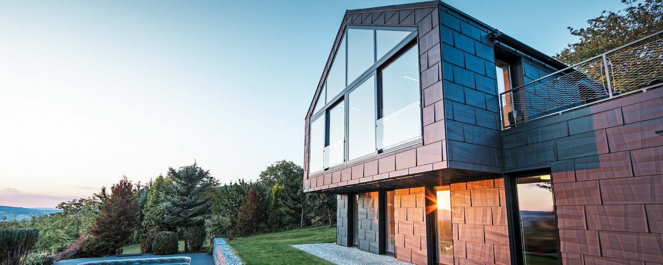 Aluminijasta fasada družinske hiše s fasadnimi ploščami PREFA FX.12 v barvi P.10 antracit ob sončnem zahodu. 