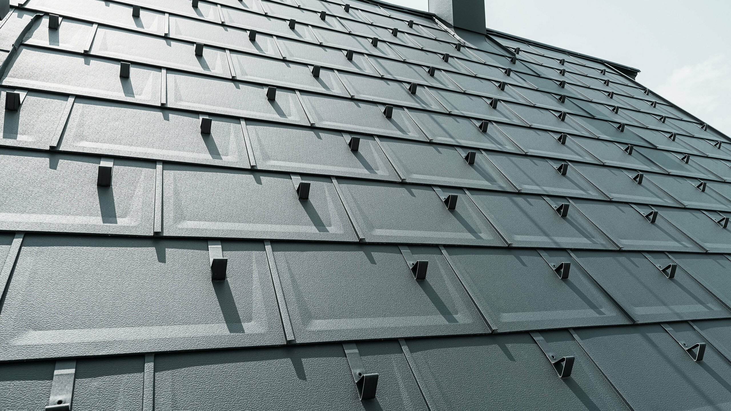 Podrobni pogled na PREFA Strešna plošča R.16 v barvi P.10 antracit. Na strehi so vidni PREFA snežni zatiči in dimnik.