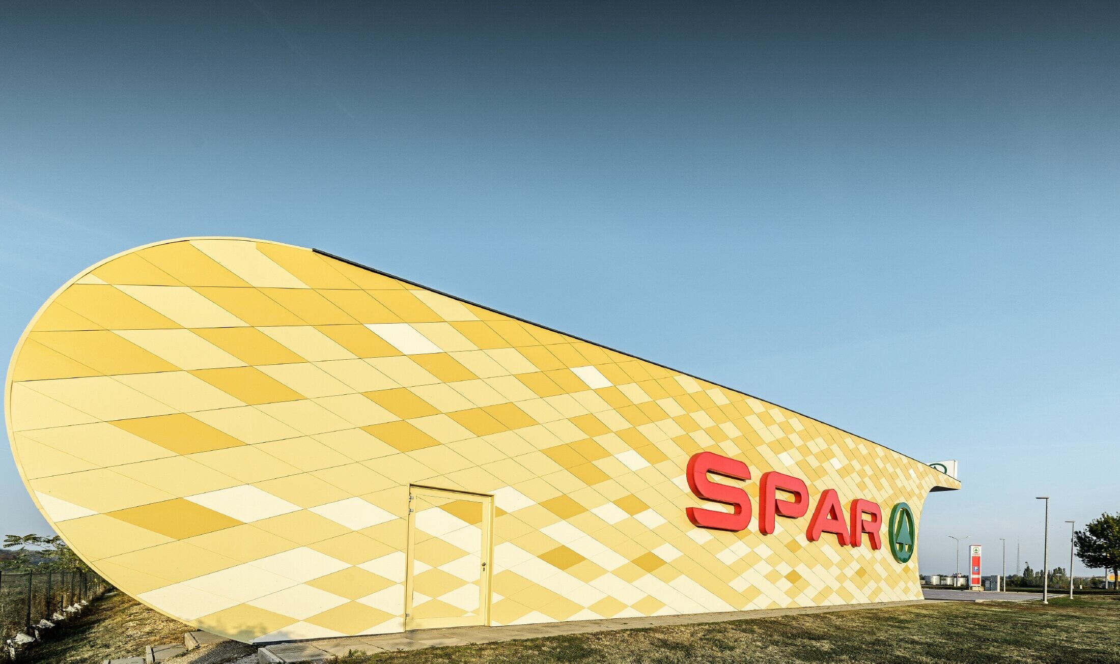 Poslovalnica Spar z aluminijasto fasado v rumeno-oranžnih karo vzorcih in logotipom Spar
