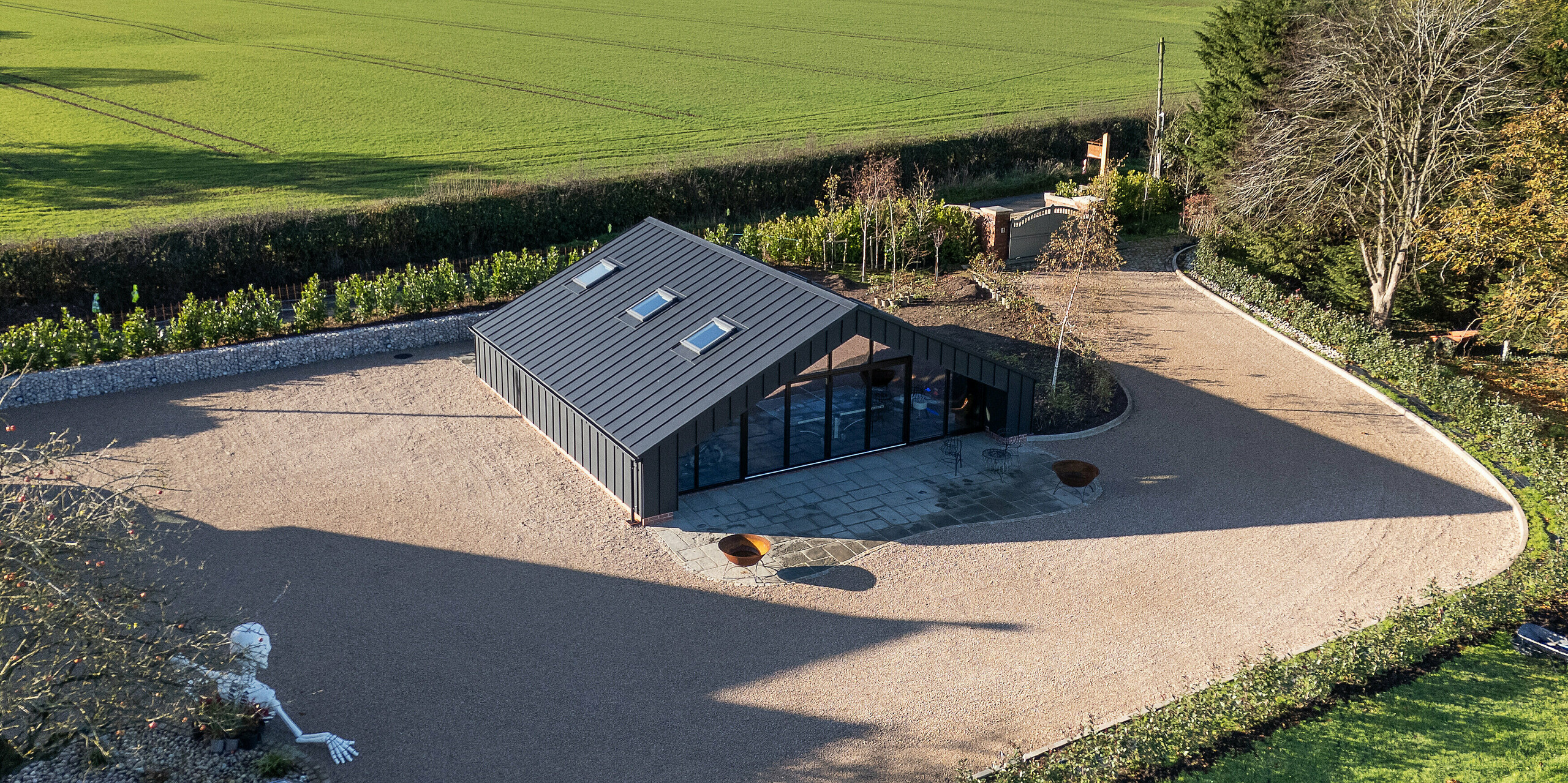 Weitläufige Vogelperspektive auf das moderne Freizeitgebäude mit vollständig verkleideter PREFA Aluminiumfassade und PREFALZ Dachflächen in P.10 Schwarz. Die präzisen Stehfalzlinien, die markante Dachgeometrie und die großflächige Glasfront setzen starke architektonische Akzente. Die robuste, witterungsbeständige Aluminiumhülle fügt sich harmonisch in die offene Landschaft ein.