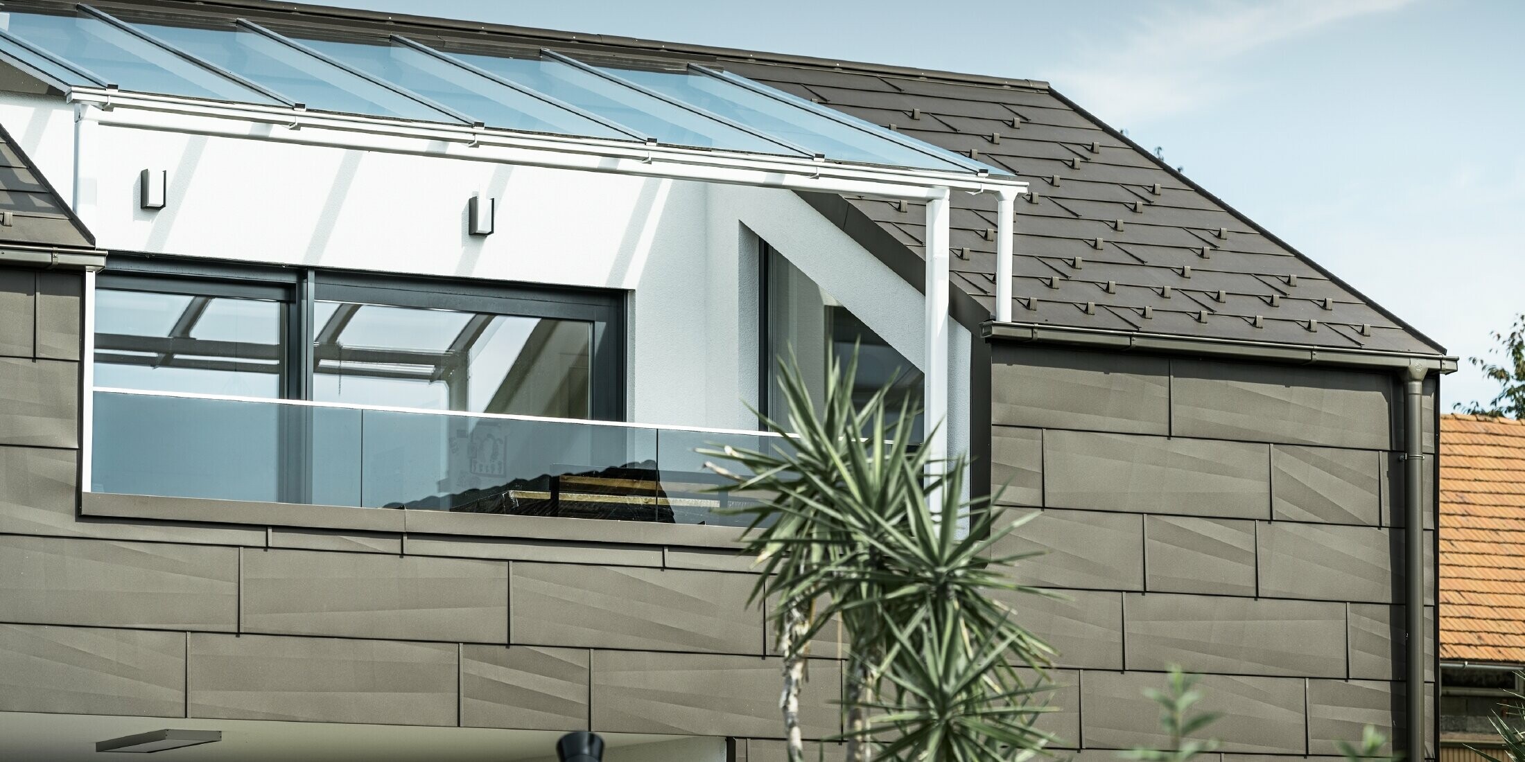 Prizidek s strešno teraso s celovitim sistemom PREFA, na strehi in fasadi so uporabljeni strešni in fasadni paneli PREFA FX.12. Poleg tega je uporabljen pravokotni žleb PREFA z odtočno cevjo in bogato paleto dodatnih elementov v rjavi barvi za odvodnjavanje strehe.