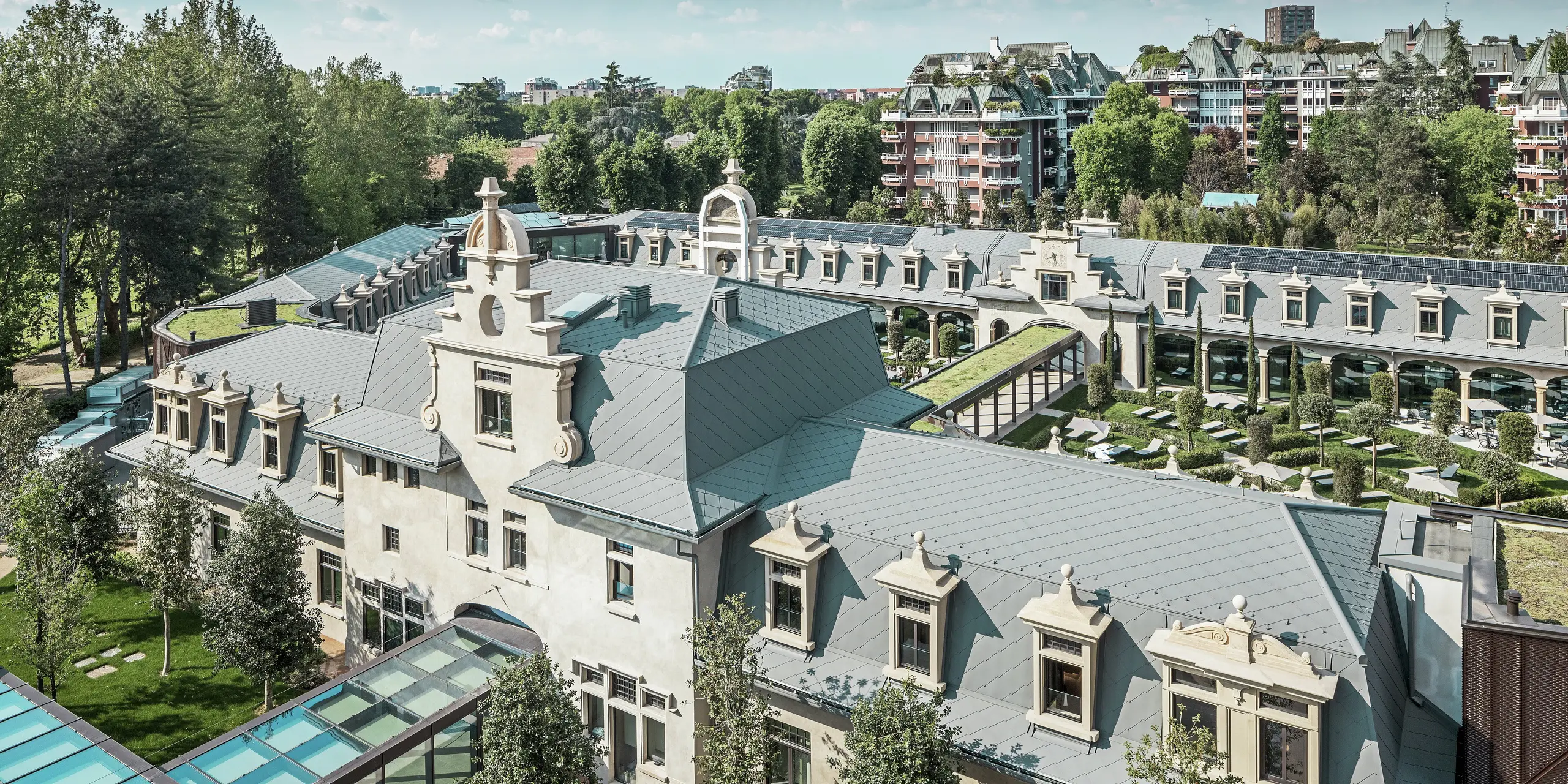 Celoten pogled na impozanten kompleks „De Montel – Terme Milano“ z arhitekturo v slogu art nouveau, ki je zaščitena kot spomenik, in sodobnim wellness ambientom. Obsežna strešna kritina s PREFA strešnimi rombi 44 × 44 v barvi P.10 svetlo siva daje kompleksu elegantno enotnost. Vgrajeni fotovoltaični moduli, zeleni strehi in steklene povezave med stavbami odražajo zahteve po trajnosti in sodobnem dizajnu v urbanem kontekstu.