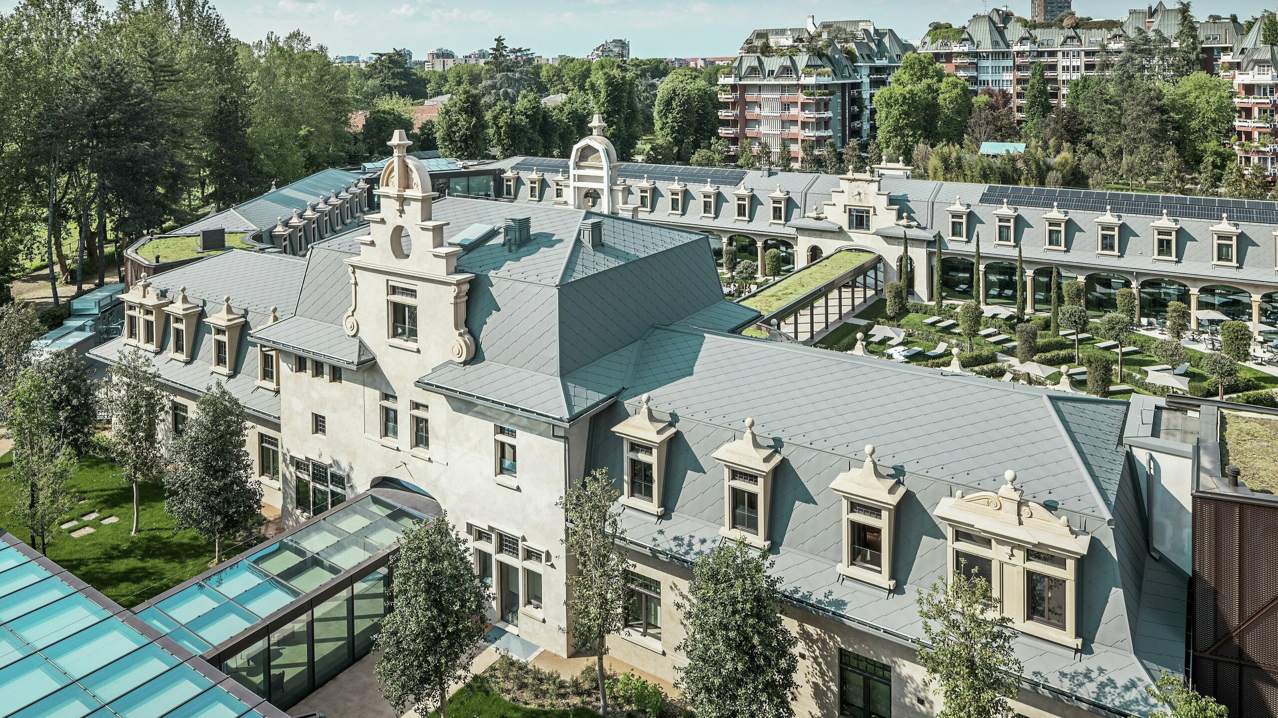 Celoten pogled na impozanten kompleks „De Montel – Terme Milano“ z arhitekturo v slogu art nouveau, ki je zaščitena kot spomenik, in sodobnim wellness ambientom. Obsežna strešna kritina s PREFA strešnimi rombi 44 × 44 v barvi P.10 svetlo siva daje kompleksu elegantno enotnost. Vgrajeni fotovoltaični moduli, zeleni strehi in steklene povezave med stavbami odražajo zahteve po trajnosti in sodobnem dizajnu v urbanem kontekstu.