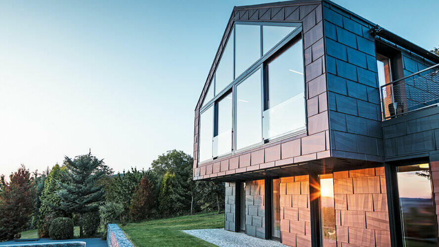 Moderna enodružinska hiša brez napušča z velikimi okenskimi površinami in fasado iz panelov FX.12 v antracitni, fotografirana ob sončnem zahodu.
