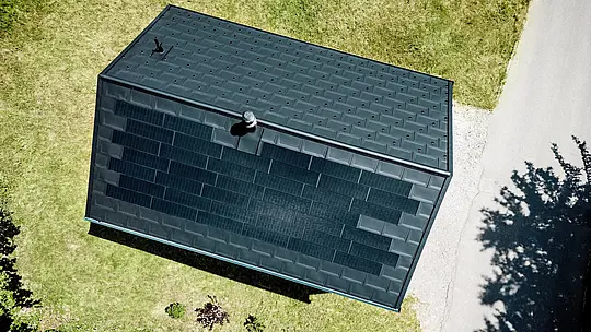 Spektakularni posnetek z dronom prikazuje PREFA solarno streho hiše Immi iz ptičje perspektive. Črne solarne strešne plošče se skoraj neopazno prelivajo v strešne plošče R.16 v barvi P.10 črna in tvorijo neprekinjeno strešno površino. Integriran aluminijasti sistem združuje trajnostno proizvodnjo sončne energije, visoko odpornost in čisto arhitekturo brez vizualno izstopajoče fotovoltaične naprave v alpskem prostoru.