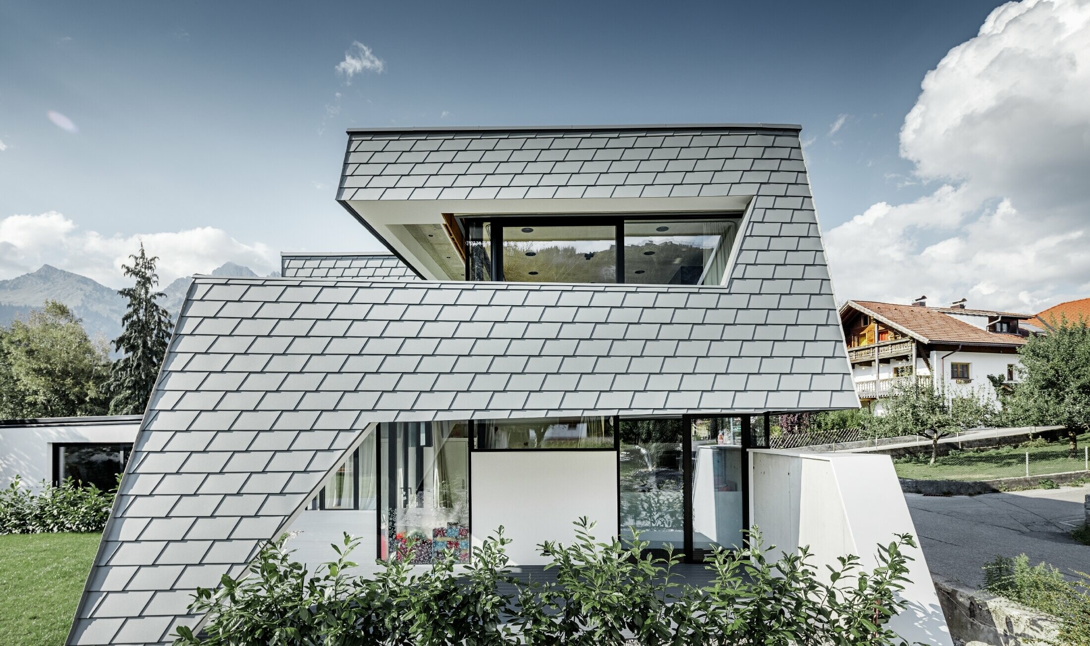 Sodobna enodružinska hiša z ravno streho, velikimi okni in fasado iz aluminijastih skodel PREFA v svetlo sivi barvi