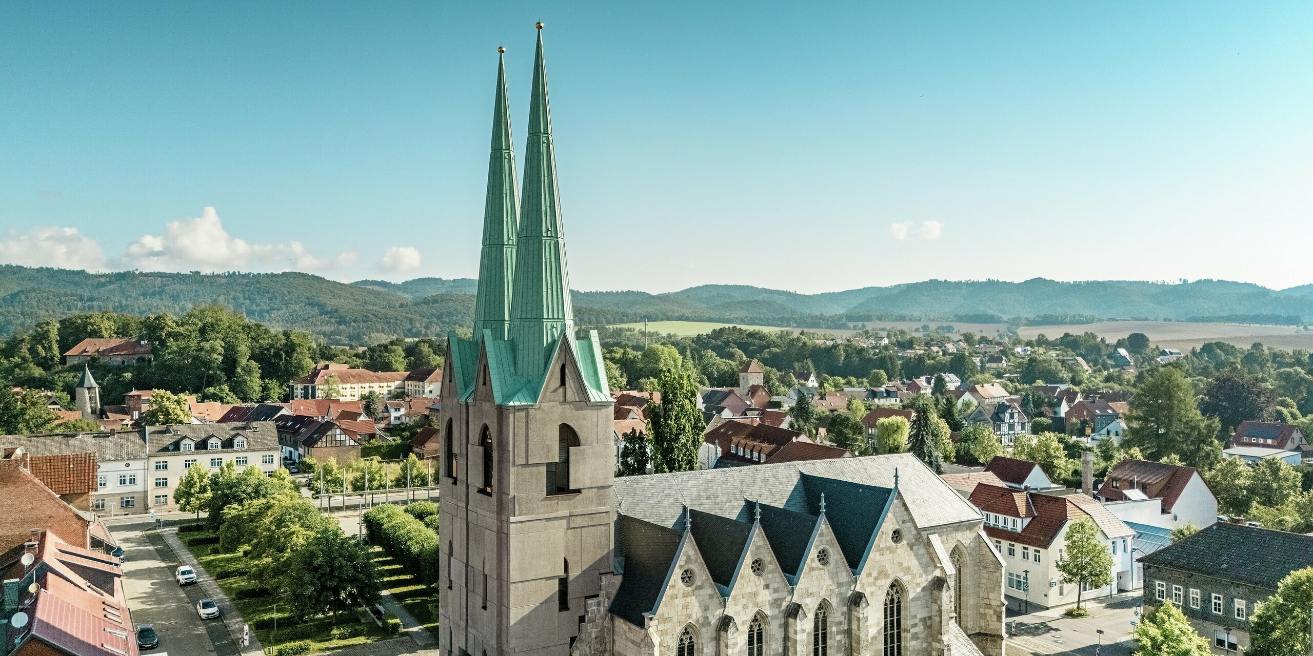 Luftaufnahme des sanierten Tourismuszentrums in Ellrich mit seiner imposanten Kirchenarchitektur. Die beiden schlanken Turmspitzen, die mit PREFALZ in der Farbe P.10 Patinagrün verkleidet sind, stechen eindrucksvoll aus dem Stadtbild hervor. Das witterungsbeständige Aluminiumdach verbindet historische Ästhetik mit moderner Technik und ist ein starkes Statement für nachhaltige Architektur.