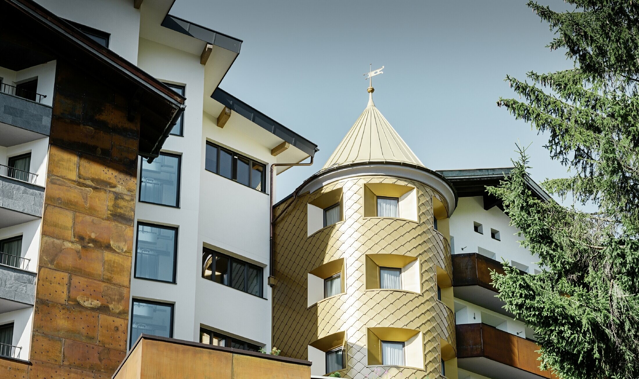 Tradicionalen hotel v kraju Ischgl z lesenimi balkoni in leseno fasado ter stolpom s pozlačenimi aluminijastimi rombi PREFA