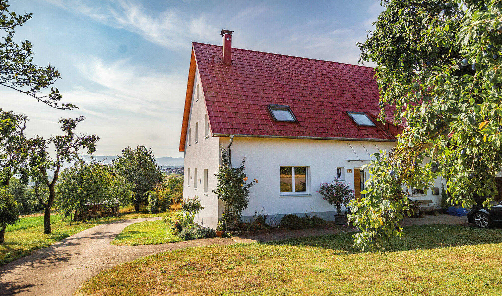 Romantisches Häuschen am land mit viel Bäumen und Sträuchern. Eingedeckt mit einem PREFA Dach in Oxydrot.