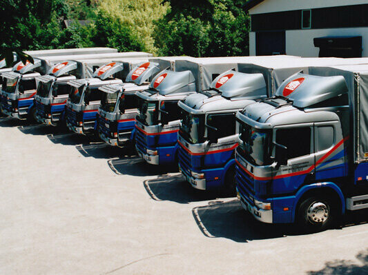 Acht ehemalige PREFA LKWs in Blau und Silber mit PREFA Logo stehen in einer Reihe 