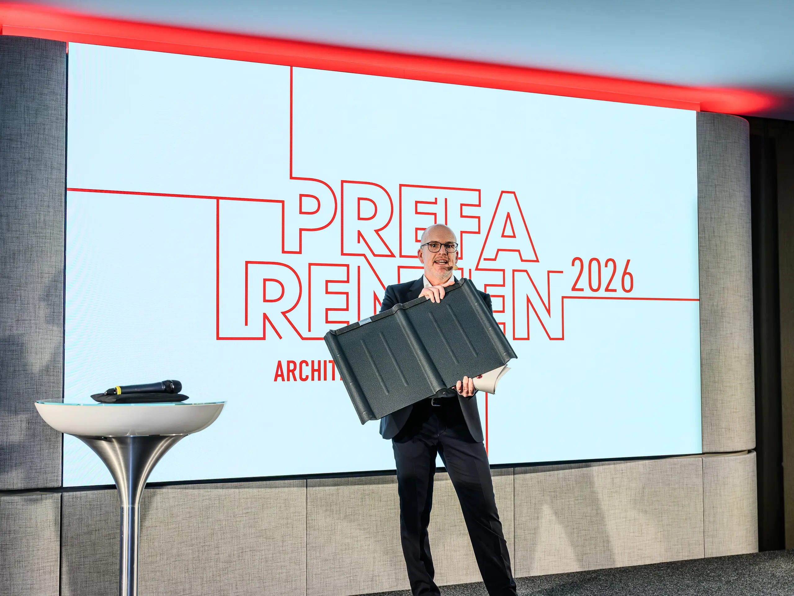 Vrhunec predstavitve PREFARENZEN 2026: Jürgen Jungmair, vodja mednarodnega marketinga PREFA, ponosno predstavlja legendarno strešno ploščo PREFA. V središču pozornosti je trajen aluminijasti izdelek, ki se uspešno proizvaja že skoraj 80 let. Sodobni oder z izrazitim logotipom PREFARENZEN poudarja pomen izdelka za prihodnostno usmerjeno arhitekturo. Lahka, odporna na nevihte, nerjavna – PREFA strešna plošča združuje tehnologijo in estetiko na najvišji ravni.