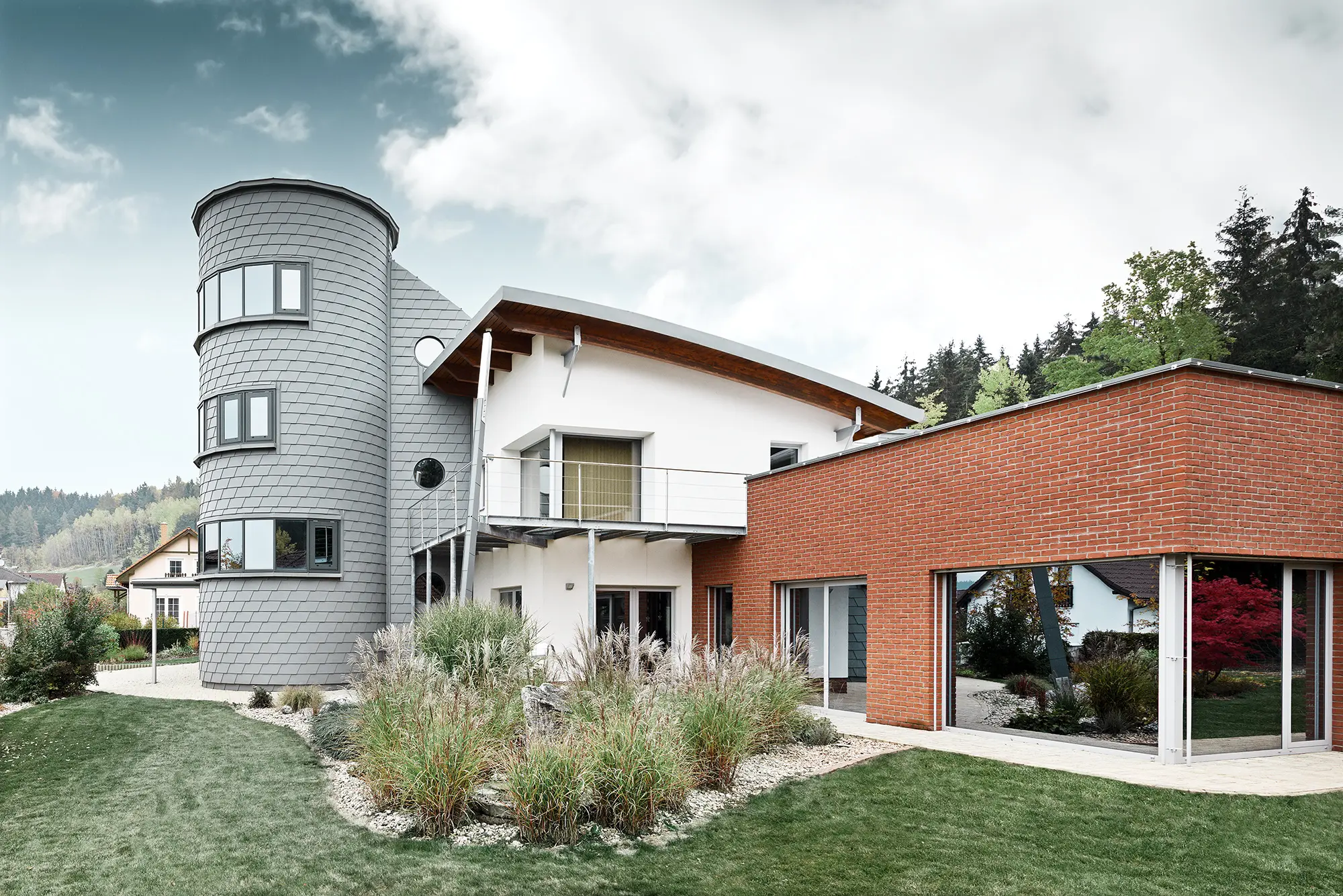 Enodružinska hiša s prizidkom v obliki stolpa, ki je obložen s fasadno skodlo PREFA v patinirano sivi barvi 