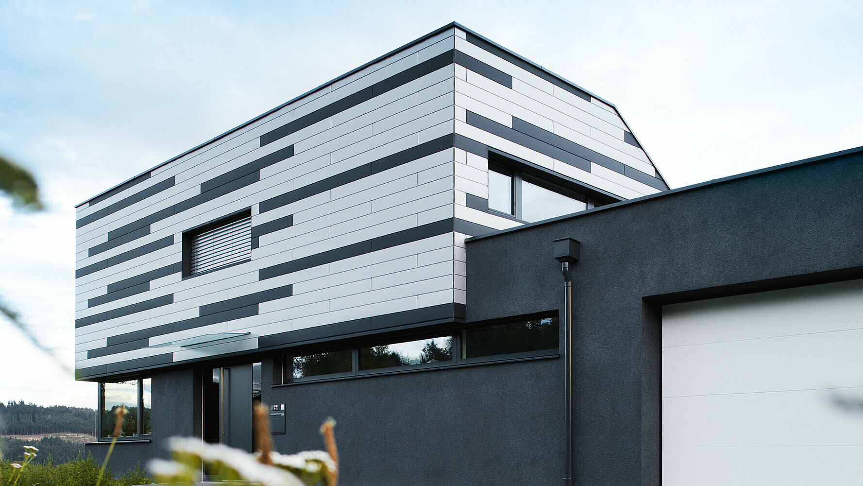 Moderna enodružinska hiša z ustvarjalno oblikovano fasado; Elementi PREFA Siding so položeni mešano v srebrni in antracitni mat.