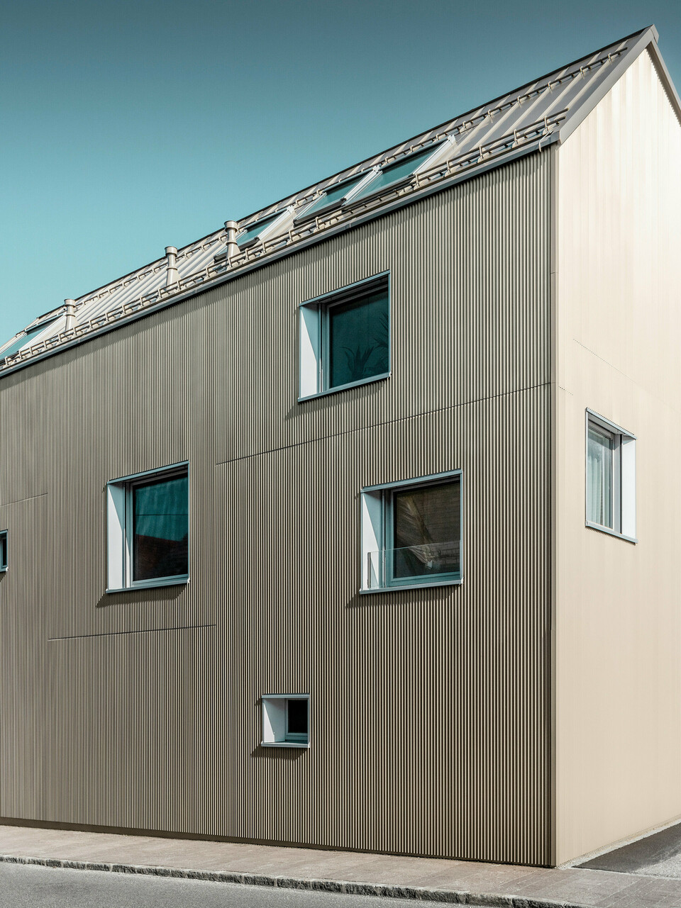 Ein modernes Einfamilienhaus in Frankenburg, Österreich zeichnet sich durch eine klare, rechtwinklige Formensprache und eine einheitliche Fassadengestaltung in Form des PREFA Zackenprofils in Bronze aus. Diese Profile verleihen der Oberfläche Struktur und Tiefe, während sie im Tageslicht changierende Schattierungen und eine ansprechende Textur hervorbringen. Das Dach ist mit PREFALZ in einer passenden Farbgebung bedeckt, was die homogene und zeitgenössische Ästhetik unterstützt. Die unregelmäßig platzierten Fenster unterbrechen die Fassade gezielt und ermöglichen Einblicke sowie natürliches Licht im Inneren, ohne die minimalistische Ausstrahlung zu beeinträchtigen.