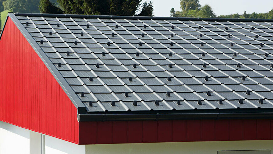 Obloga zatrepa v rdeči z navpično montiranimi aluminijastimi elementi PREFA Siding. Na strehi so montirane PREFA strešne plošče v P.10 antracitni.