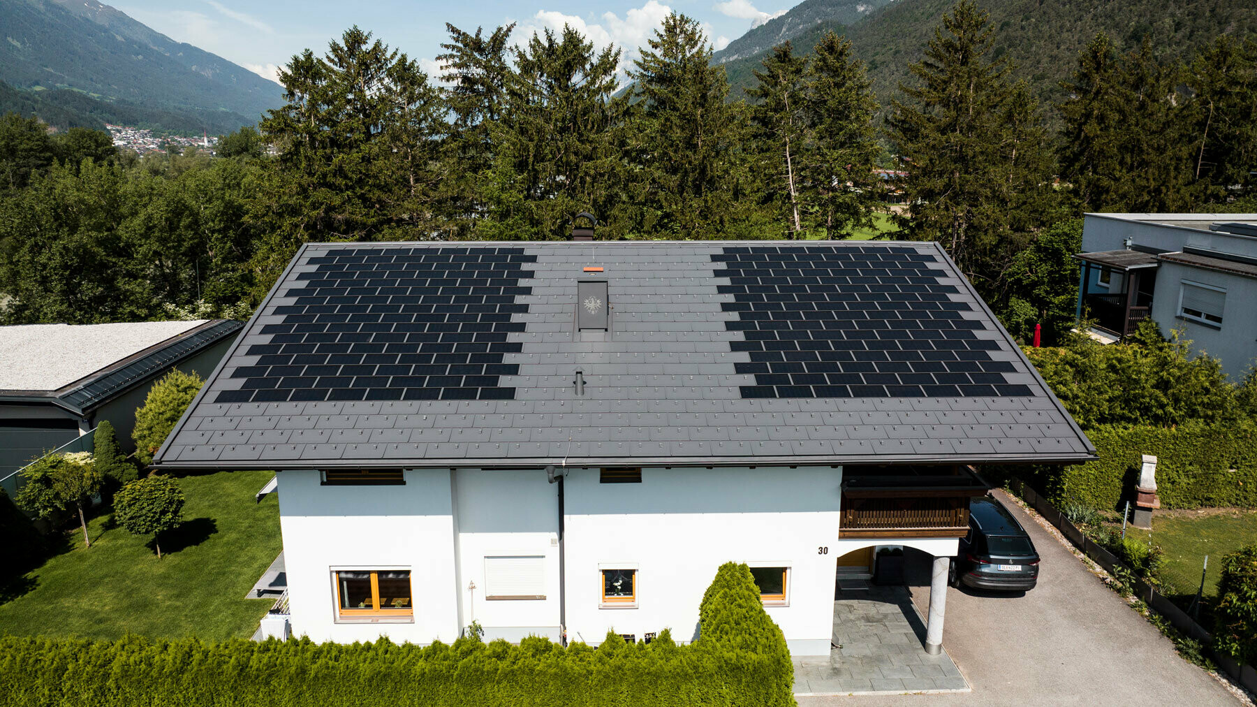 Prikazana je enodružinska hiša v podeželskem okolju, pokrita z malo solarno strešno ploščo PREFA s strešno ploščo R.16 v barvi P.10 temno siva.