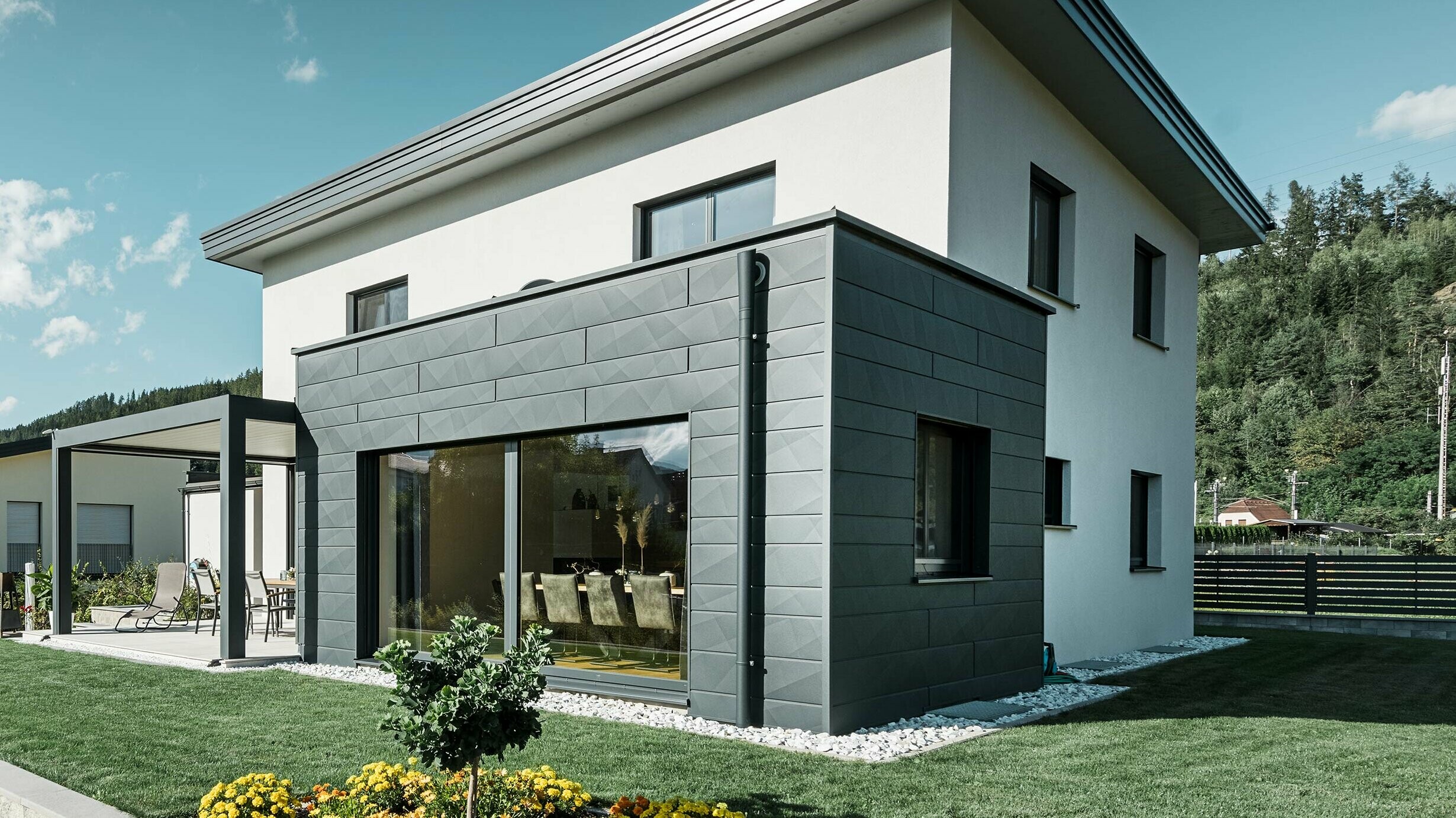 Enodružinska hiša s prizidkom, prizidek je izveden z aluminijasto fasado PREFA, odvodnjavanje ravne strehe je izvedeno z nastavkom za izliv PREFA in odtočno cevjo PREFA v barvi P.10 antracit,