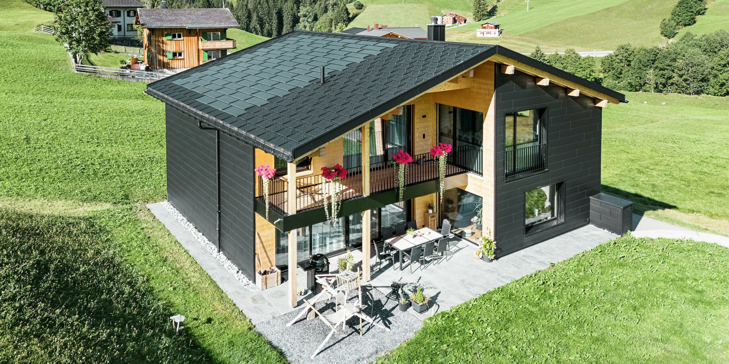 Elegantna enodružinska hiša v hribovitem okolju Ascharina (Švica) kaže, kako se lahko aluminij in les odlično združita. Robustni fasadni paneli PREFA Siding.X v črni barvi P.10 so usklajeni s streho iz solarnih strešnih plošč PREFA in strešnih plošč R.16 v enakem barvnem premazu. Trpežna aluminijasta obloga zanesljivo ščiti stavbo pred izzivi alpskega podnebja.